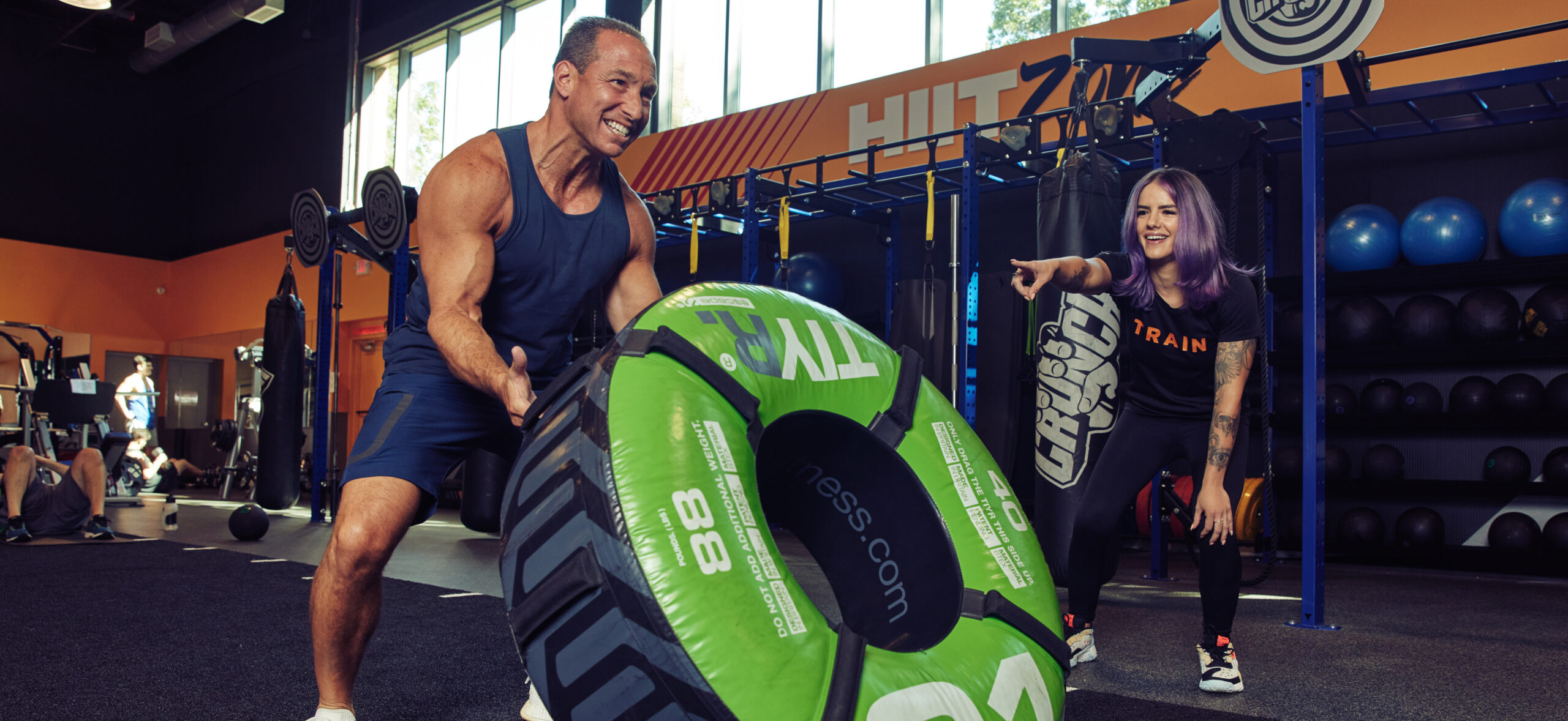 Man using a tire with the help of a personal trainer